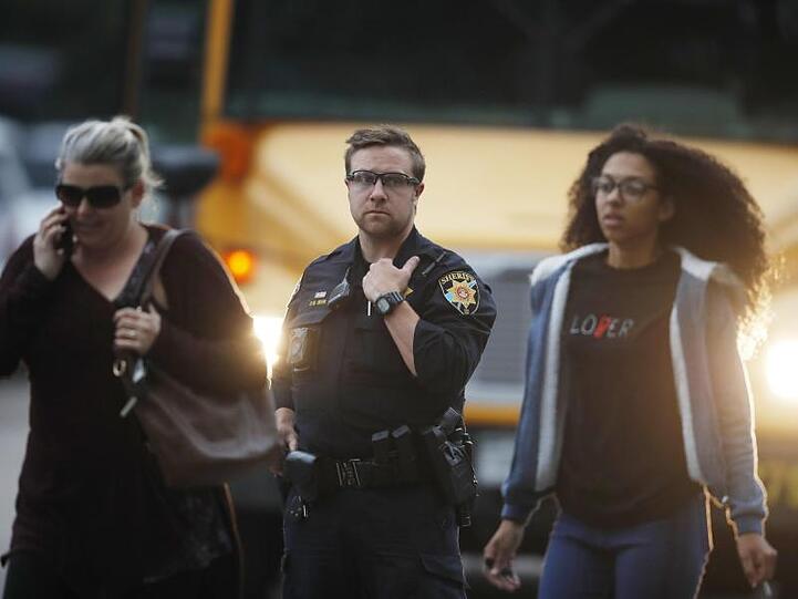 Ein Polizist schützt nach der Bluttat Schüler, die vor der angegriffenen Highschool aus einem Bus steigen.