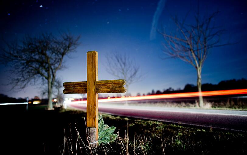 Ein Kreuz und Blumen erinnern am Straßenrand an einen Verkehrstoten.