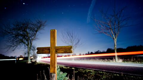 Ein Kreuz und Blumen erinnern am Straßenrand an einen Verkehrstoten.