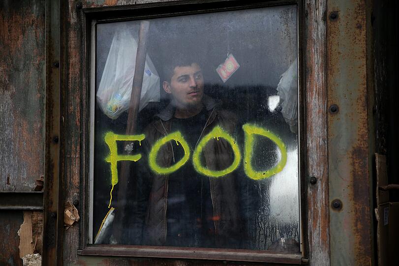 14.01.2017: Quälend langes Warten in der eisigen Kälte: Ein Flüchtling steht in einer Lagerhalle in Belgrad (Serbien) an einem Fenster mit der Aufschrift "Food".