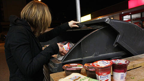 Eine junge Frau fischt heimlich Lebensmittel aus der Abfalltonne eines Supermarktes &ndash; das nennt man "Containern".