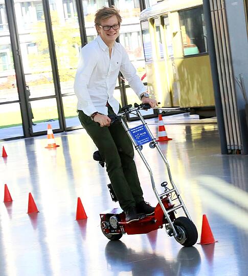 Tim auf dem E-Scooter. Kaum zu sehen aber wahr: Der hat sogar einen Sitz - und ist fürchterlich schwer.