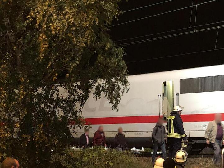 Rettungskräfte helfen Bahn-Passagieren bei ihrem Weg aus dem liegengebliebenen ICE 1272 zu einer Bushaltestelle.