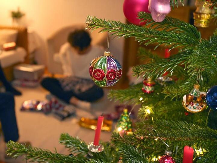 Eine Junge packt hinter einem geschmücktem Christbaum Weihnachtsgeschenke aus.