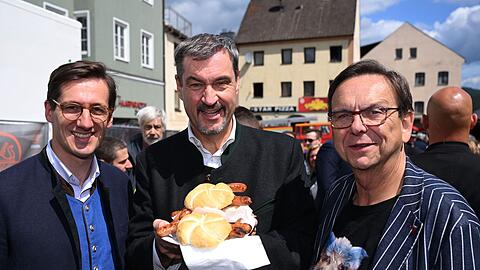 Markus Söder (M.) hält Bratwurst-Semmeln in die Kamera.
