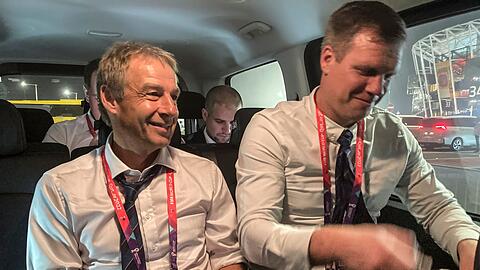 Jürgen Klinsmann (l) sitzt in einem Auto, während er einen Podcast aufnimmt.