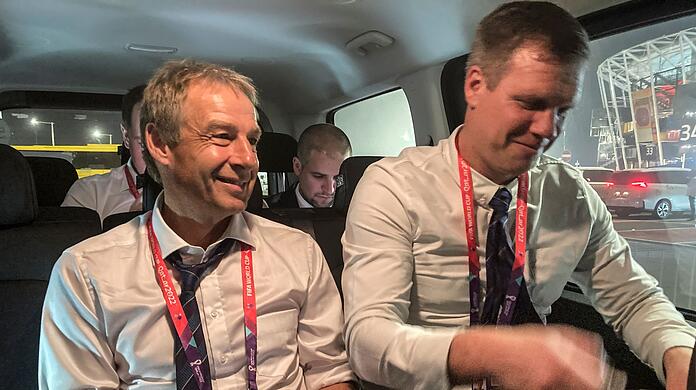 Jürgen Klinsmann (l) sitzt in einem Auto, während er einen Podcast aufnimmt.