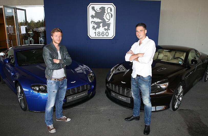 Die Löwen-Profis Benny Lauth (l.) und Stefan Buck posieren vor zwei Aston-Martin-Sportwagen. Die Marke soll auch nächste Saison noch auf der Löwen-Brust prangen.
