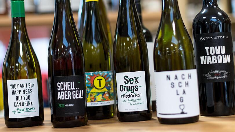 Weine mit kreativ gestaltete Etiketten und/oder originellen Namen stehen in einem Weinhandel auf einem Tisch.