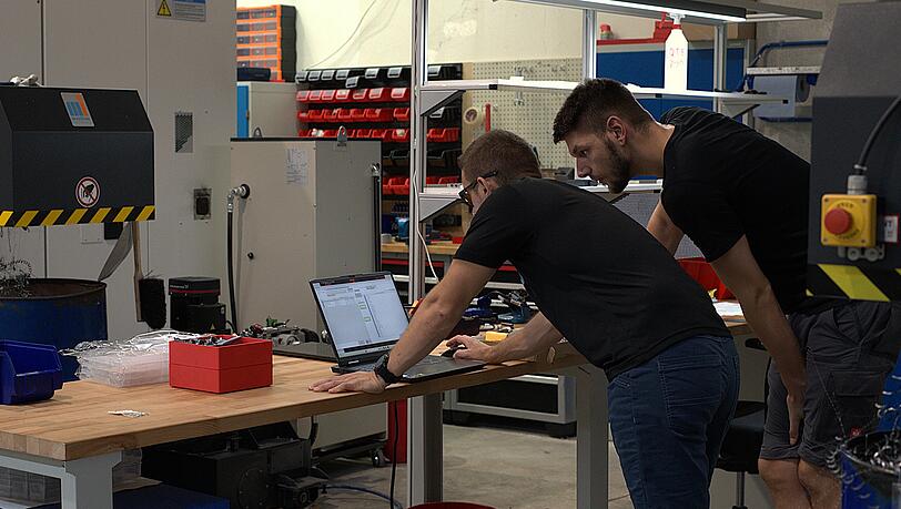 Zwei Mitarbeiter von Deltavision arbeiten in der Produktionshalle. In deren Zentrum: die CNC-Maschine, welche die Teile fertigt. Zwei Mitarbeiter von Deltavision arbeiten in der Produktionshalle. In deren Zentrum: die CNC-Maschine, welche die Teile fertigt.