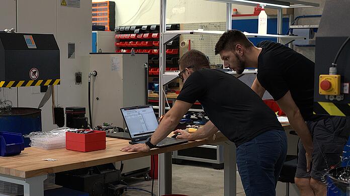 Zwei Mitarbeiter von Deltavision arbeiten in der Produktionshalle. In deren Zentrum: die CNC-Maschine, welche die Teile fertigt. Zwei Mitarbeiter von Deltavision arbeiten in der Produktionshalle. In deren Zentrum: die CNC-Maschine, welche die Teile fertigt.