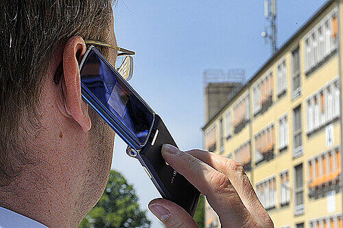 Ein Mann telefoniert mit seinem Handy  in der Nähe eines Mobilfunkmastens