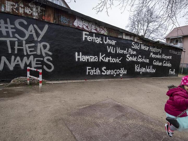 Ein kleines Mädchen schaukelt vor der Wand eines Jugendzentrums, auf dem die Namen der Opfer des Anschlags vom 19. Februar geschrieben stehen.