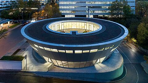 Beleuchtet im Abendlicht sieht die neue Betriebs-Kita der HypoVereinsbank wie ein Ufo aus - im Hintergrund das ikonische, denkmalgeschützte Hypo-Hochhaus von 1981, auch HVB-Tower genannt.