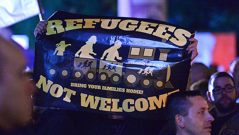 Demonstranten halten ein Plakat mit der Aufschrift "Refugees not welcome" nach oben. Demonstranten halten ein Plakat mit der Aufschrift "Refugees not welcome" nach oben.