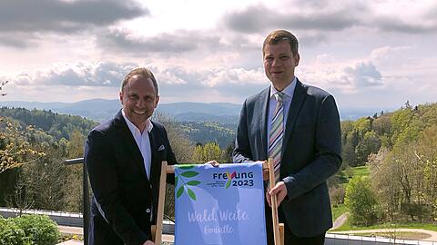 Bayerns Umweltminister Thorsten Glauber (Freie Wähler, r) und der Bürgermeister der Stadt Freyung, Olaf Heinrich (CSU), halten einen Liegestuhl mit dem Logo der Landesgartenschau 2023.