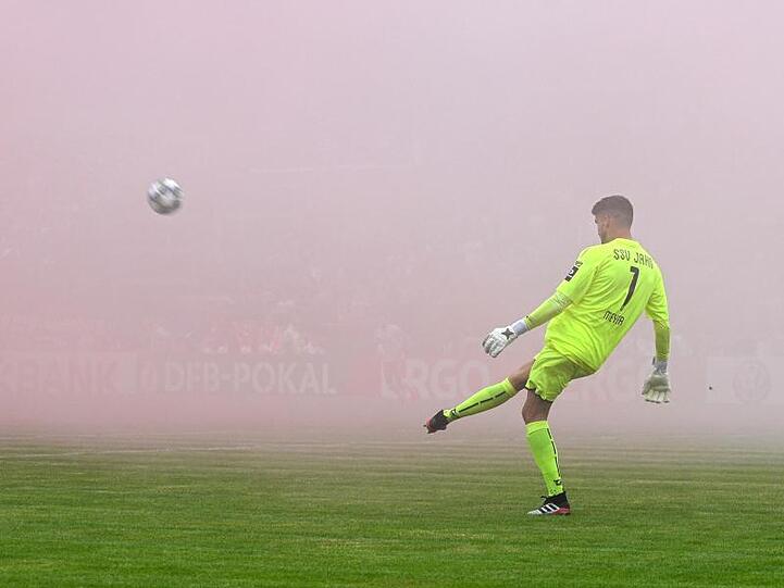 Regensburgs Torhüter Alexander Meyer schießt den Ball vor Rauch von Bengalischen Feuern. Foto: Oliver Dietze