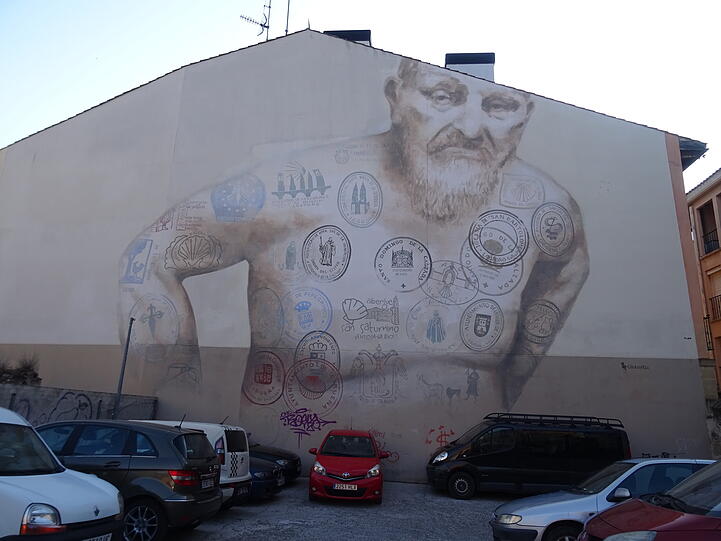 Übergroßes Wandbild auf einer Häuserwand in Logroño. Als Tattos sind zahlreiche Pilgerstempel des Camino Francés zu sehen.