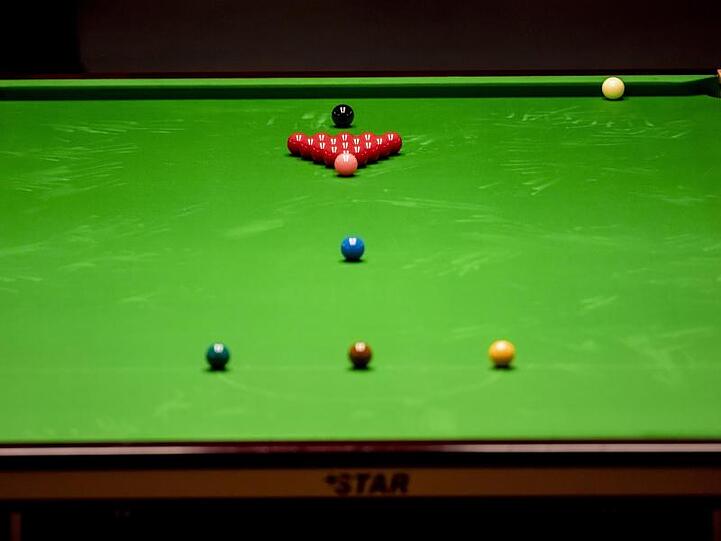 Snookerkugeln und Queues liegen auf einem Snookertisch bereit.