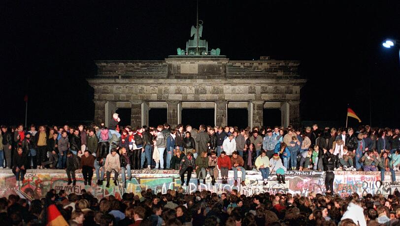 Ein Bild, das um die Welt ging: Jubelnde Menschen sitzen am 9. November 1989 auf der Mauer am Brandenburger Tor.