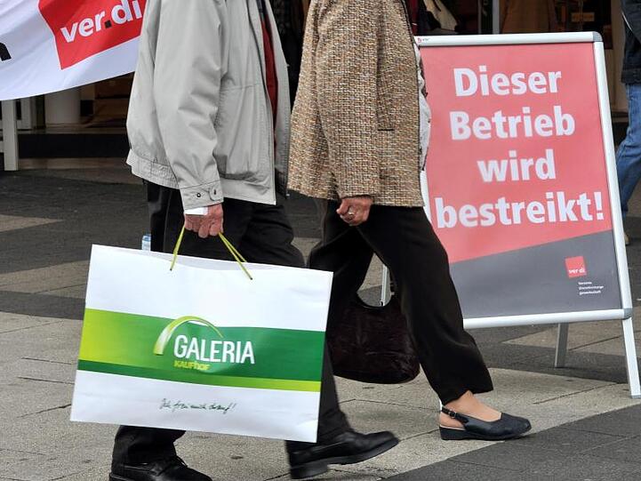 Ein Kunde mit einer Galeria-Kaufhof-Tüte geht an einer Kaufhof-Filiale vorbei, die bestreikt wird. Foto: Uwe Zucchi/dpa
