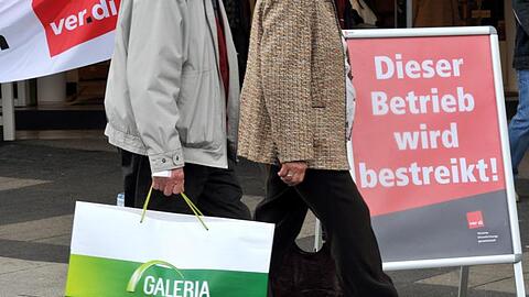 Ein Kunde mit einer Galeria-Kaufhof-Tüte geht an einer Kaufhof-Filiale vorbei, die bestreikt wird. Foto: Uwe Zucchi/dpa