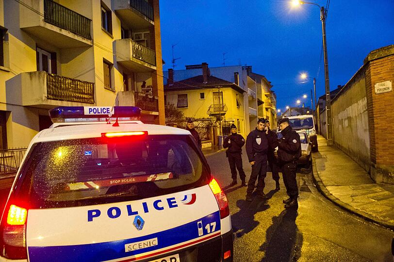 Der Tatort ist weiträumig abgeriegelt, Sanitätsfahrzeuge sowie Polizisten mit Hunden sind vor Ort, Polizisten mit schusssicheren Westen und Helmen haben das Viertel abgeriegelt.