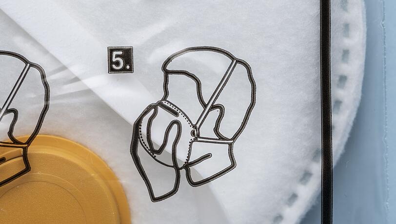 Anleitung für das korrekte Aufsetzen der Maske auf der Verpackung einer FFP3-Atemschutzmaske. (Symbolbild) Anleitung für das korrekte Aufsetzen der Maske auf der Verpackung einer FFP3-Atemschutzmaske. (Symbolbild)