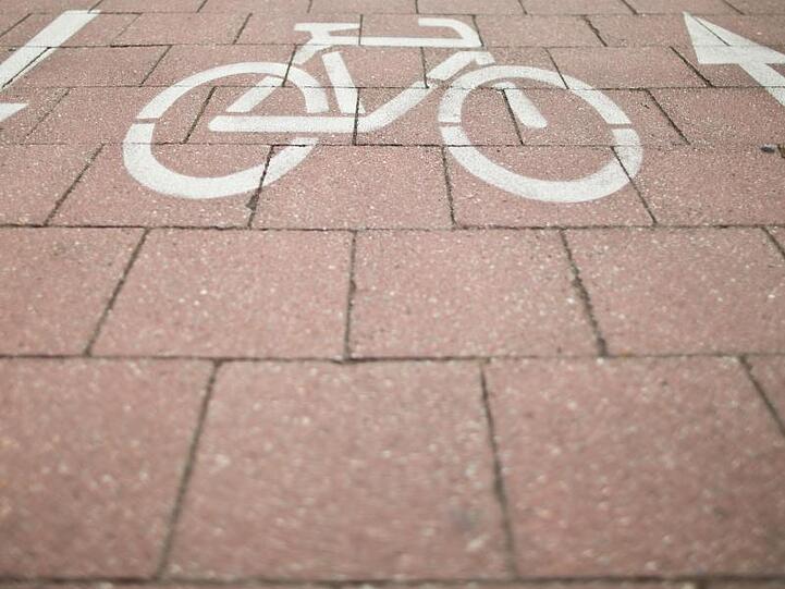 Ein Fahrradsymbol mit zwei wegweisenden Pfeilen ist auf dem Straßenboden zu sehen. Foto: picture alliance / dpa/Archivbild