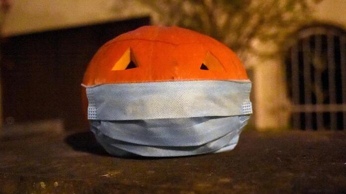 Ein Halloween-Kürbis mit einem Mundschutz liegt vor einem Haus.