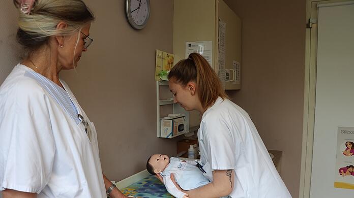 Praxiskoordinatorin Astrid Giesen (links) ist sehr zufrieden damit, wie Studentin Laura Simson das Übungspuppenbaby hoch hebt.