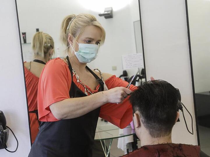 Eine Friseurin mit Mundschutz schneidet einem Kunden die Haare.