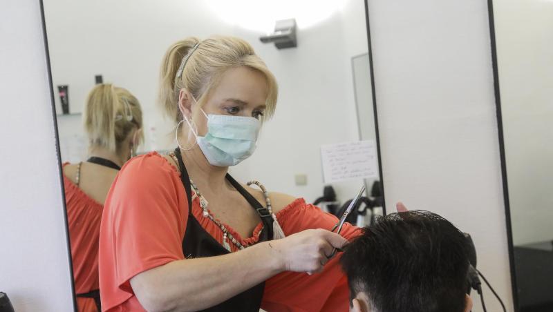 Eine Friseurin mit Mundschutz schneidet einem Kunden die Haare. Eine Friseurin mit Mundschutz schneidet einem Kunden die Haare.
