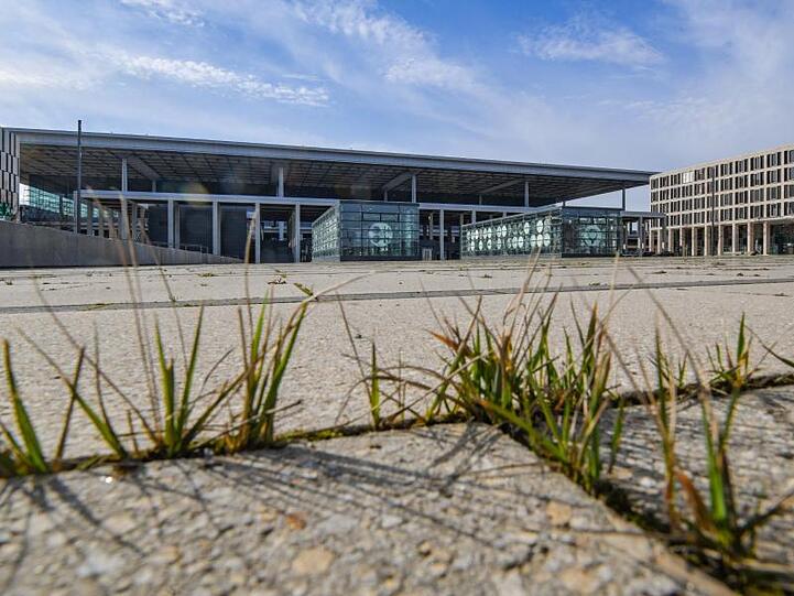 Gras wächst zwischen den Fugen auf einem Platz vor dem Terminal des Hauptstadtflughafens BER.