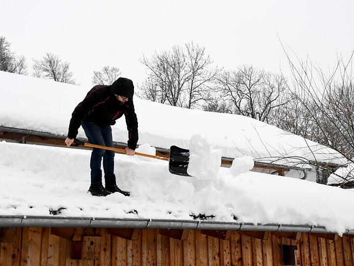Ein Mann befreit ein Dach vom Schnee. Foto: Tobias Hase