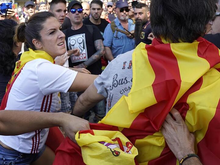 Geteiltes Spanien vor dem ersten Jahrestag des Unabhängigkeitsreferendums: Eine Frau, die eine spanische Flagge trägt, schlägt einen Mann, der sich in eine katalonische Flagge gehüllt hat.