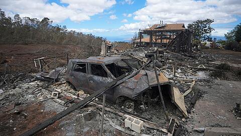 Die verkohlten Überreste eines Fahrzeugs stehen  in Kula neben einem von einem Waldbrand zerstörten Haus.