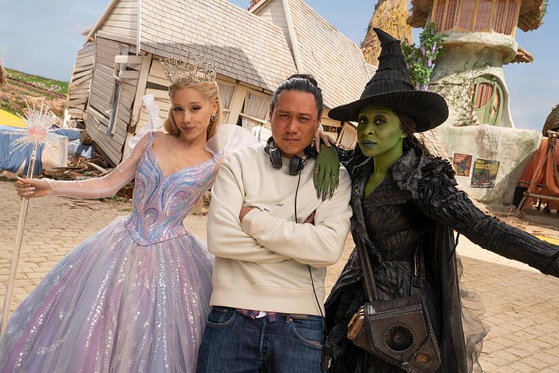 Die Gute und Böse Fee rahmen den Regisseur ein: Ariana Grande (als Glinda), Jon M. Chu, und Cynthia Erivo (als Elphaba).