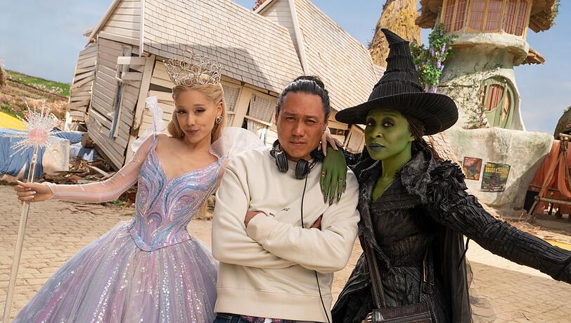 Die Gute und Böse Fee rahmen den Regisseur ein: Ariana Grande (als Glinda), Jon M. Chu, und Cynthia Erivo (als Elphaba).