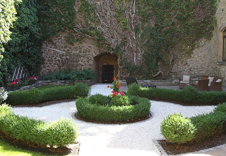Eine stilvolle Oase: der kleine Schlossgarten auf Schloss Guttenberg mit einer gemütlichen Sitzecke und roten Rosen.