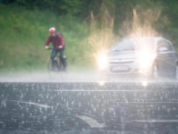 Ein Radfahrer fährt im prasselndem Regen neben einem Auto her.