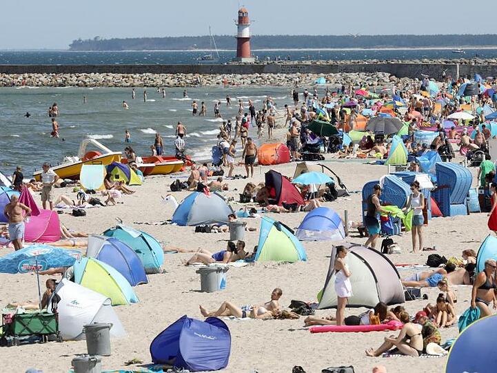 Am Ostseestrand von Warnemünde herrscht Hochbetrieb. Strandmuscheln und Sonnenschirme bestimmen das Bild.