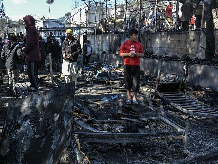 Flüchtlinge stehen im Lager Moria auf den abgebrannten Überresten eines Containerhauses.