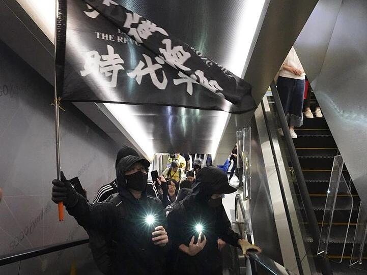 Demonstranten mit Mundschutz tragen eine Flagge mit der Aufschrift "Befreit Hongkong, die Revolution unserer Zeit" in einem Einkaufszentrum.