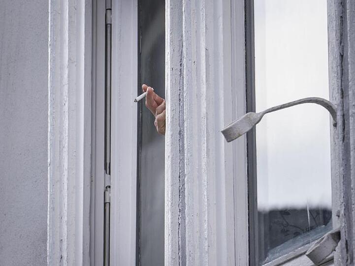Ein Mann raucht während der Ausgangsbeschränkung am Fenster.