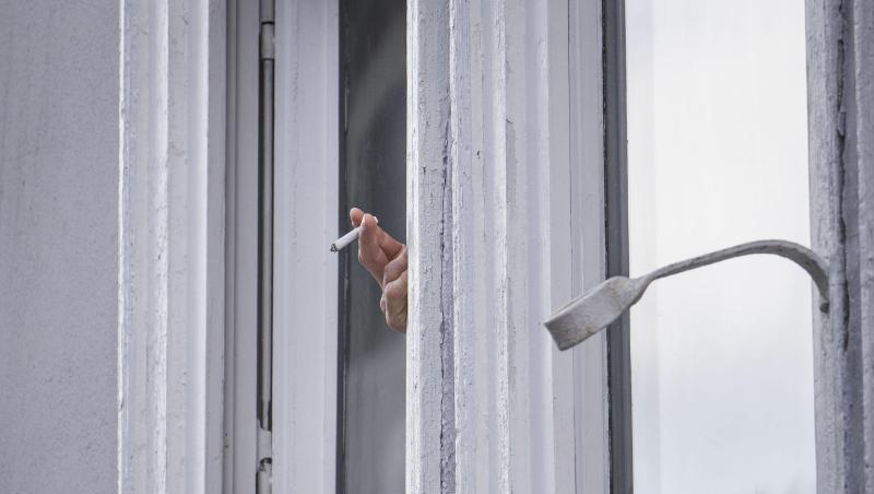 Ein Mann raucht während der Ausgangsbeschränkung am Fenster. Ein Mann raucht während der Ausgangsbeschränkung am Fenster.