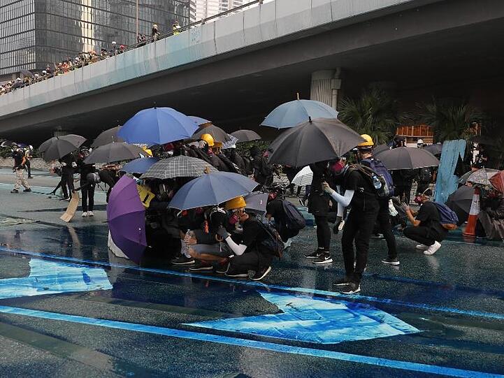 Vor dem blau eingefärbten Wasser schützen sich Demonstranten mit Regenschirmen.