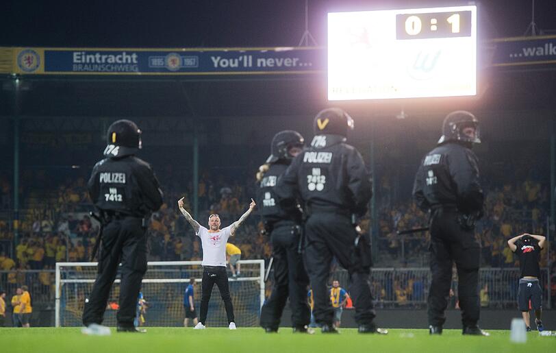 Braunschweiger Fans stehen Polizisten und Ordnern nach dem Abpfiff auf dem Platz gegenüber.