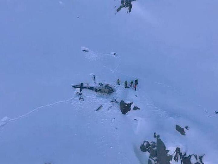 Eine Gruppe von Bergrettern stehen neben den Trümmern des Hubschraubers.