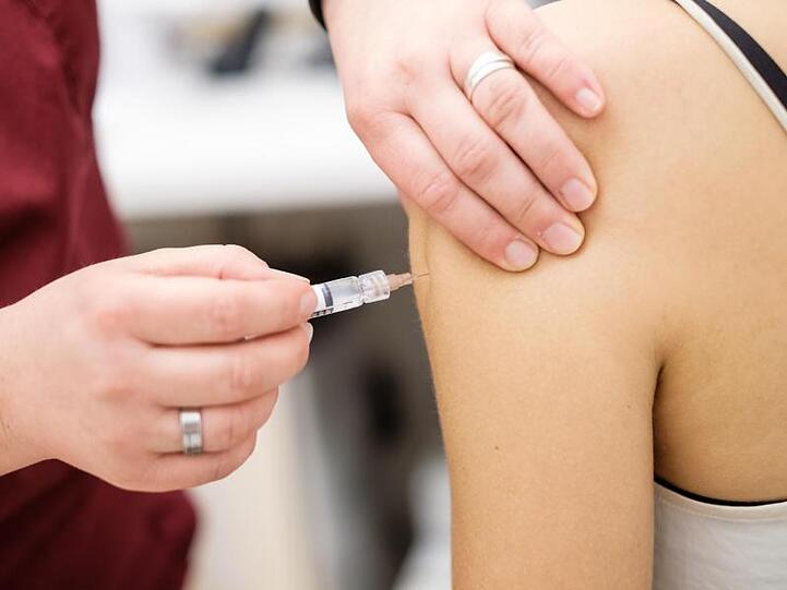 Eine Arzthelferin impft in einer Arztpraxis eine junge Patientin mit einer Spritze.
